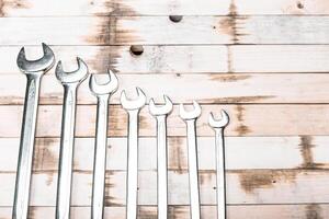 Various sizes of metal wrenches arranged on a wooden surface for tool organization and identification photo