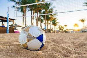 Beach soccer ball resting on warm sand with palm trees in the background during sunset photo