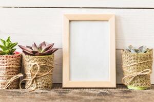 Decorative planters with succulents and a blank frame on a rustic wooden surface in a cozy interior setting photo