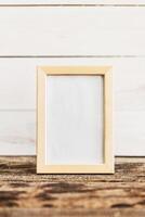 Empty picture frame displayed on a rustic wooden surface against a white wooden background photo