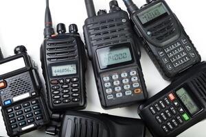 Diverse collection of handheld radios and communication devices arranged on a white surface photo