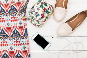 Stylish summer outfit laid out on a white wooden surface with accessories and a smartphone charging photo