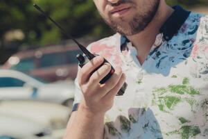 Man using a walkie-talkie wearing a colorful shirt in a parking lot during a sunny day photo