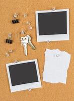 Blank photo frames on corkboard with keys and office supplies scattered around in a creative workspace