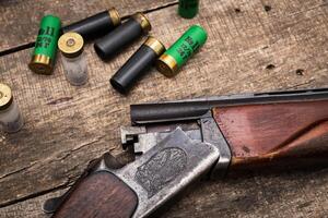 Classic shotgun resting on a wooden surface surrounded by various shotgun shells in a rustic setting photo