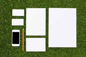 Various sizes of blank paper and a smartphone arranged on green grass for creative planning and brainstorming photo