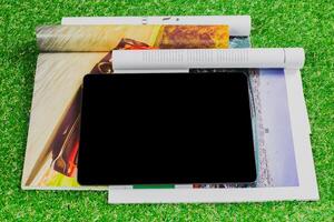 Tablet resting on magazines with a green grass background during a bright daytime leisure setting photo