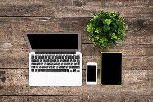 Working environment on wooden desk with laptop, smartphone, tablet, and potted plant photo