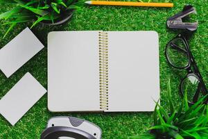 Open notebook surrounded by office supplies and greenery on a faux grass surface during a creative work session photo