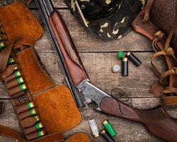 Hunting gear and shotgun displayed on rustic wooden surface with ammunition and accessories photo
