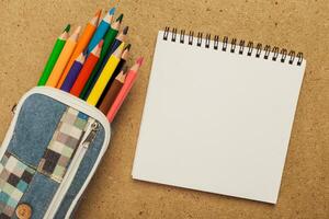 Colorful pencils and blank notepad on textured background ready for creative drawing or note-taking activity photo