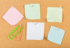 Colorful sticky notes and paper clips arranged on a cork board with push pins during a daylight workspace setup photo