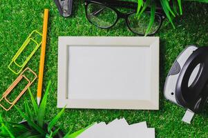 Workspace setup with blank picture frame, stationery, and greenery during daylight hours photo