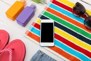 Summer beach essentials arranged on a colorful towel with sunscreen bottles and a smartphone photo