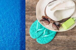 Summer essentials for a relaxing day by the pool with flip flops, sunglasses, sunscreen, and a straw hat on a wooden surface photo