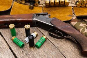 Vintage shotgun with ammunition and hunting gear arranged on a rustic wooden table in a natural setting photo