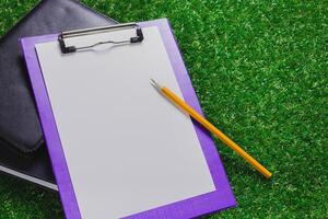 Blank clipboard and pen resting on green grass during a sunny day, ready for notes or sketches outdoors photo