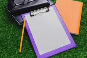 Blank notepad and clipboard ready for notes on green grass during sunny day in the park with notebooks nearby photo