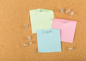 Colorful sticky notes pinned on corkboard surface with clear push pins scattered around photo