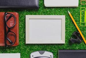 Collection of stationary items arranged on green grass with empty frame and office tools at midday photo