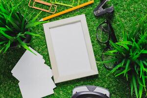 Workspace setup for creative projects with empty frame and stationery on green grass photo