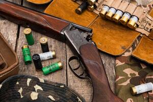 Shotgun and ammunition displayed on a rustic wooden table surrounded by hunting accessories in an outdoor setting photo