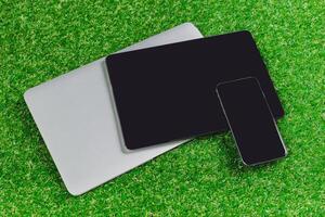 Multiple electronic devices arranged on green grass in a modern outdoor setting during daylight hours photo