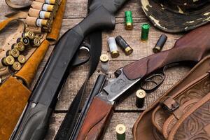 Collection of hunting firearms and ammunition displayed on a rustic wooden surface for outdoor enthusiasts photo