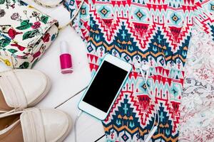 Brightly patterned summer outfit laid out with accessories and a smartphone on a light wooden surface photo