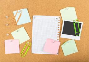 Creative workspace setup with colorful sticky notes, paper clips, and a blank notepad on a corkboard photo