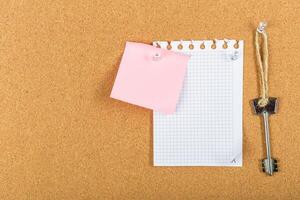 Note-taking setup with a blank grid sheet, a pink sticky note, and a vintage key on corkboard at home office workspace photo