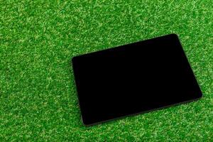 Tablet resting on artificial grass under bright sunlight during a calm afternoon in a park photo