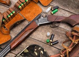 Wood and metal shotgun with ammunition on wooden table displayed for hunting enthusiasts in a rustic environment photo