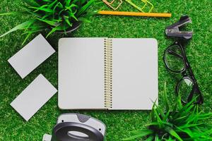 Stationery setup with blank notebook, stationery supplies, and greenery on grass background during bright daylight photo