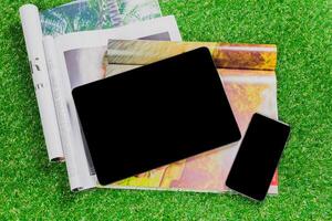 Tablet and smartphone resting on open magazines on green grass during a sunny day in a relaxing outdoor setting photo