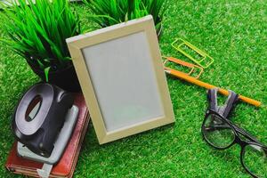 Workspace setup featuring a blank picture frame, stationery, and greenery on a tabletop in a bright environment photo