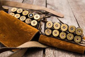 Shotgun shells and leather holder arranged on rustic wooden surface in hunting setup photo