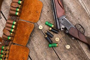 Shotgun with ammunition laid on a rustic wooden surface during a hunting trip in autumn photo