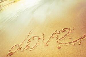 Love written in the sand at sunset on a tranquil beach with gentle waves lapping the shore photo
