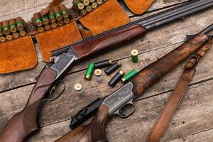 Collection of hunting shotguns and ammunition arranged on a rustic wooden table photo