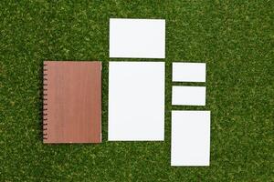 Collection of blank papers and a notebook arranged on green grass in bright sunlight photo