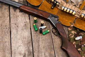 Classic shotgun and ammunition displayed on rustic wooden surface with camouflage cloth photo