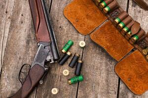 Shotgun and ammunition lay on a wooden table, highlighting hunting tools in a rustic setting photo