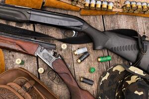 Collection of shotguns and ammunition displayed on a rustic wooden table in preparation for a hunting trip photo