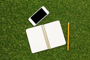 Notebook and smartphone on green grass during a sunny day for studying or brainstorming ideas photo