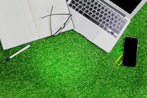 Workspace setup on artificial grass with laptop, notebook, and smartphone during a casual outdoor study session photo