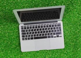 Laptop resting on green artificial grass with a reflective screen in an outdoor setting during daylight hours photo