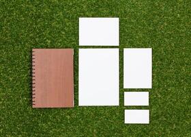 Blank stationery on green grass with a wooden notebook displaying a minimalistic workspace in natural light photo