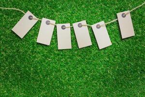 Blank tags hanging on a string over green artificial grass background photo