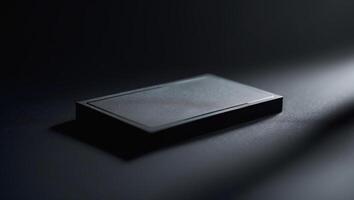 Black rectangular device rests on a dark surface, illuminated by a soft light in a minimalistic setting photo